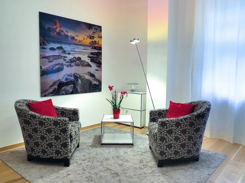 Empty clinic consultation room with chairs, table, and wall artwork.